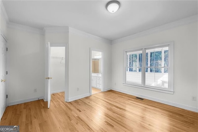 unfurnished bedroom with crown molding, a spacious closet, connected bathroom, light hardwood / wood-style floors, and a closet