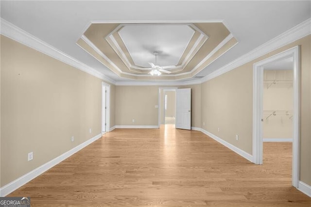 empty room featuring a raised ceiling, ceiling fan, light wood-type flooring, and ornamental molding