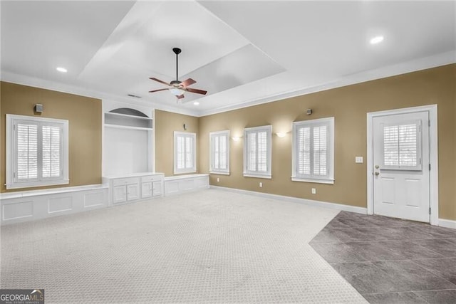 unfurnished living room with a raised ceiling, ceiling fan, crown molding, and carpet floors