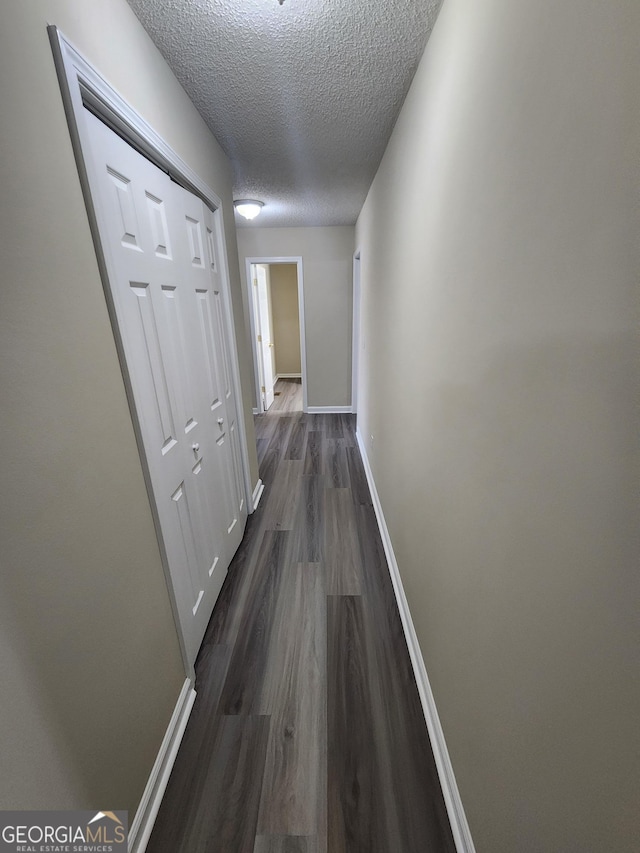 corridor featuring dark wood-style floors, a textured ceiling, and baseboards