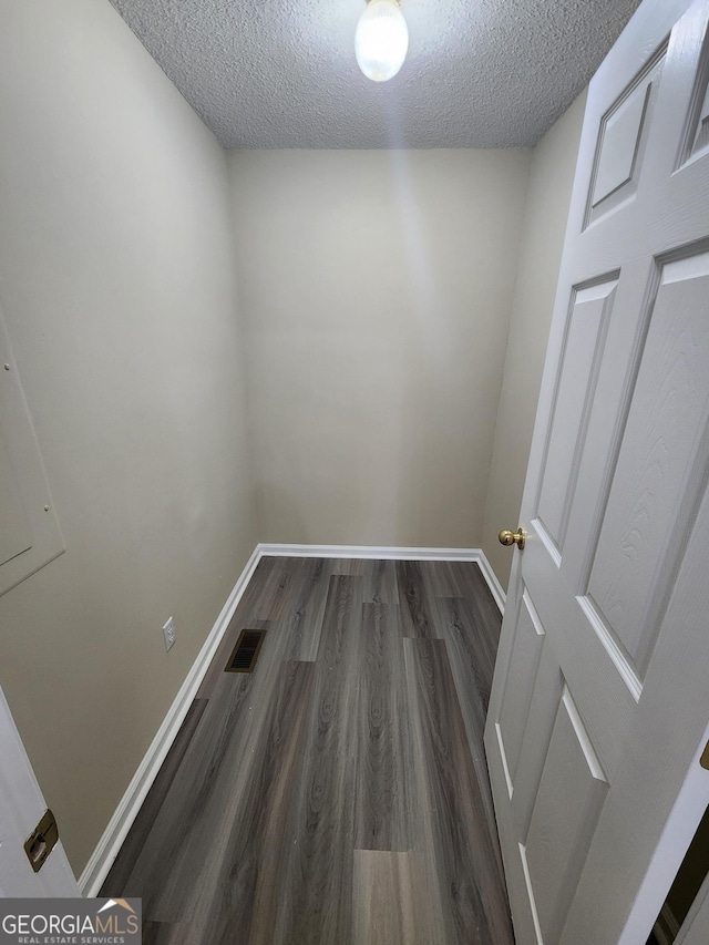 laundry area with dark wood-type flooring, visible vents, a textured ceiling, and baseboards