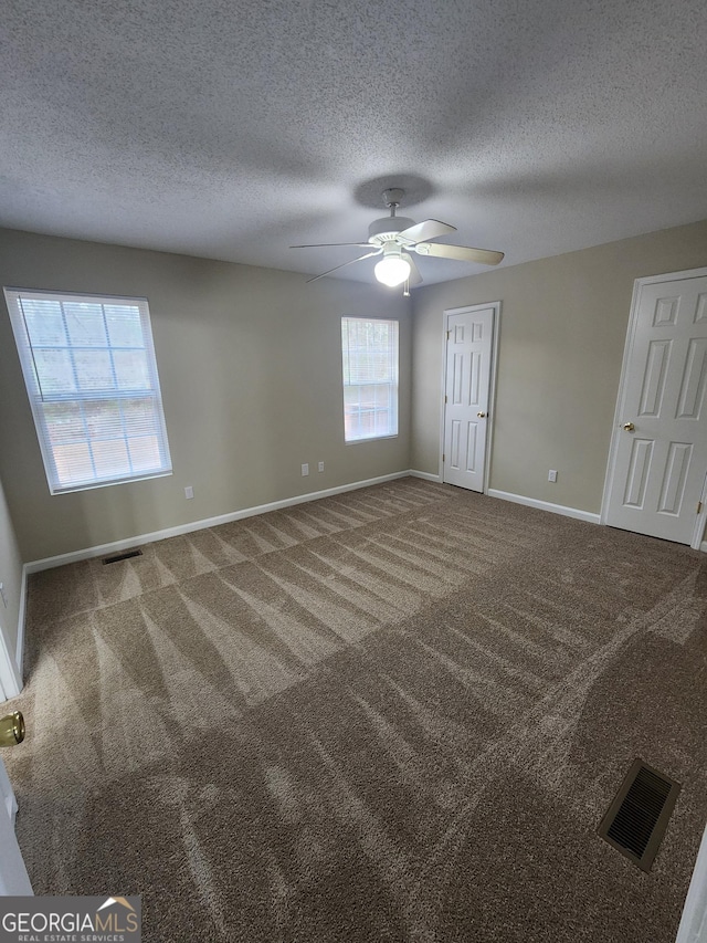 carpeted empty room featuring baseboards, visible vents, and a textured ceiling