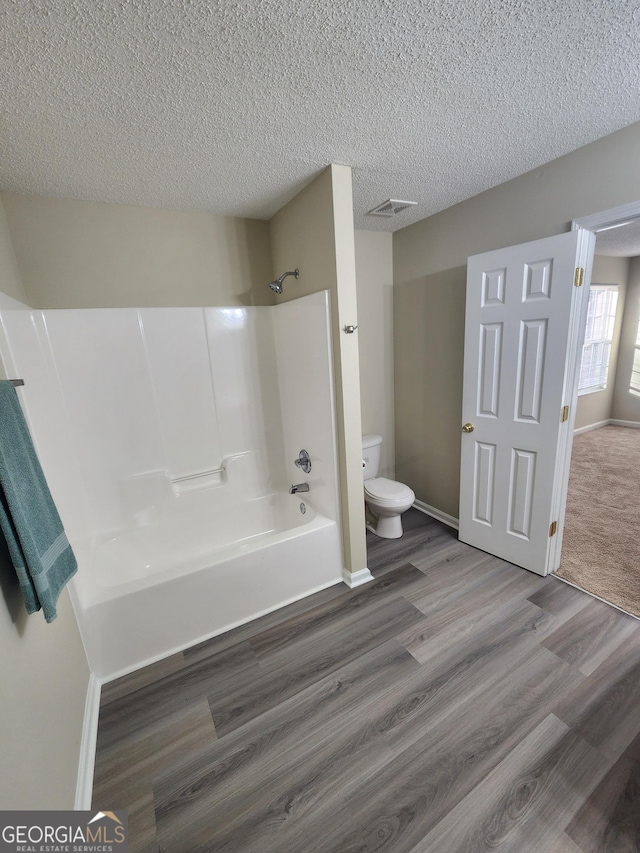 bathroom featuring shower / bathtub combination, a textured ceiling, toilet, wood finished floors, and visible vents