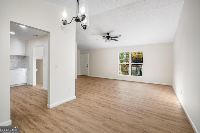 unfurnished living room with a textured ceiling, light hardwood / wood-style flooring, and ceiling fan with notable chandelier