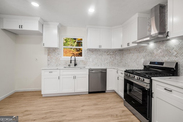 kitchen featuring light stone countertops, white cabinetry, sink, stainless steel appliances, and wall chimney range hood