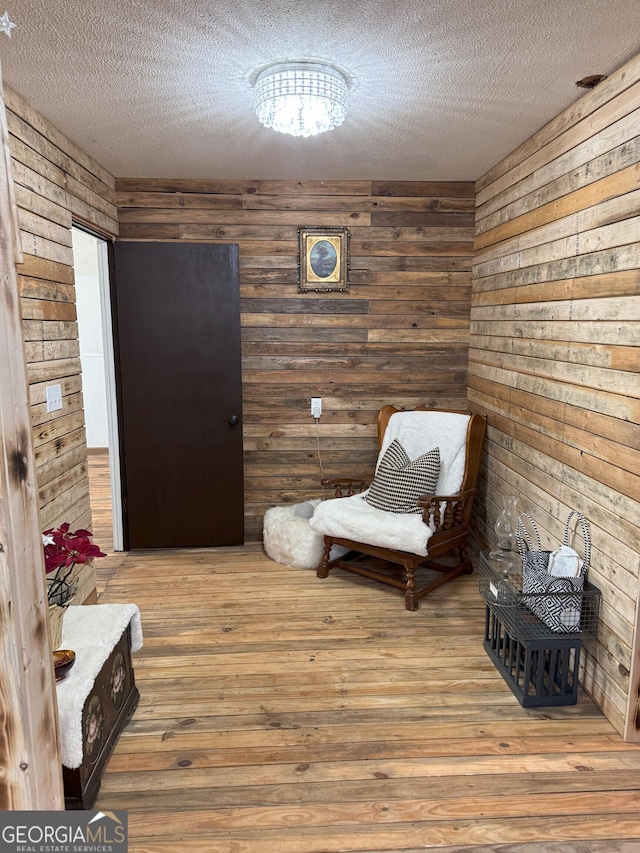 sitting room featuring a textured ceiling, hardwood / wood-style flooring, wood walls, and a notable chandelier