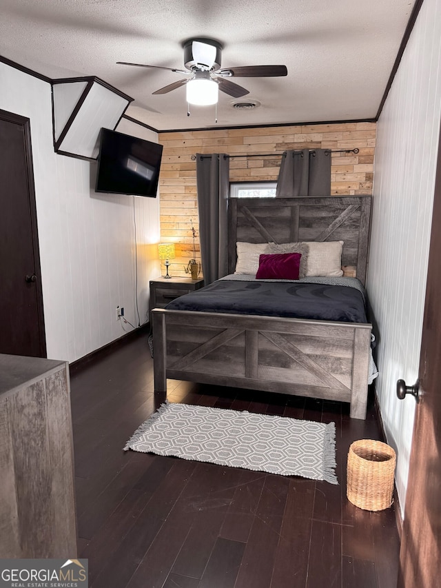 bedroom featuring ceiling fan, dark hardwood / wood-style flooring, wooden walls, and a textured ceiling