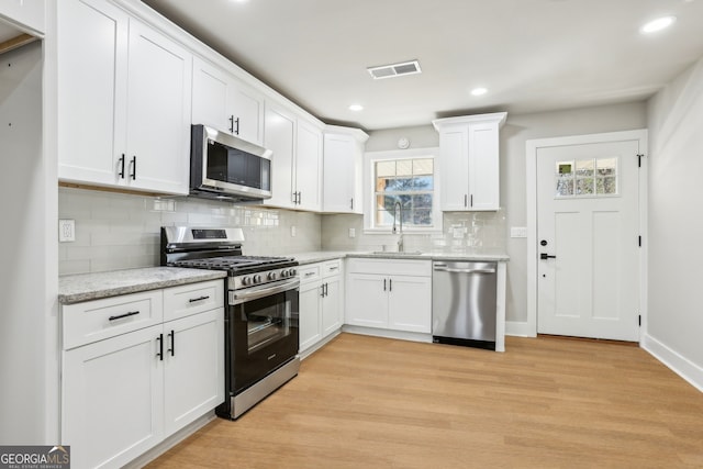 kitchen with sink, white cabinets, light stone counters, light hardwood / wood-style flooring, and appliances with stainless steel finishes