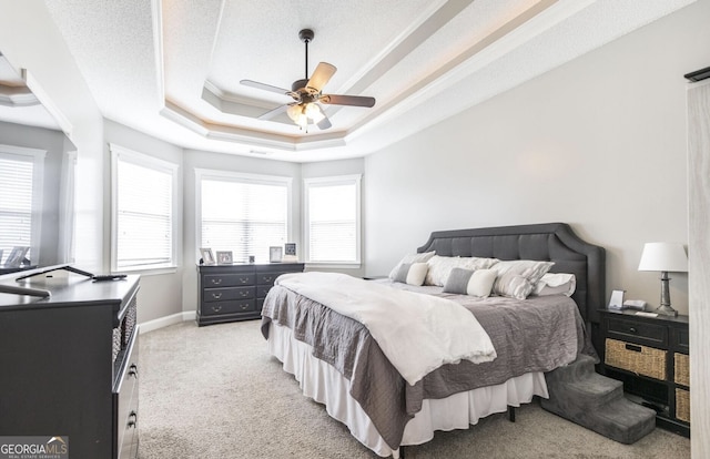 bedroom with a textured ceiling, a tray ceiling, ceiling fan, and light colored carpet