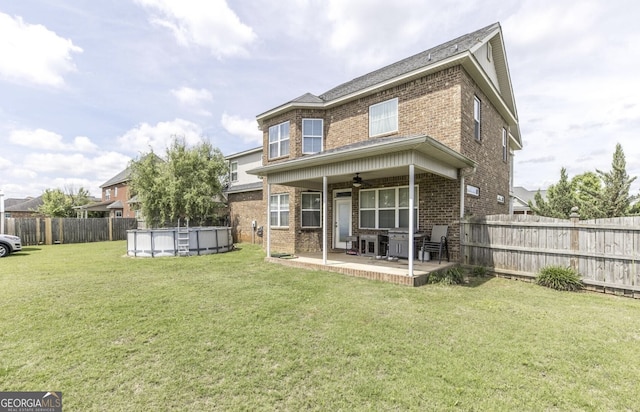 rear view of property featuring a fenced in pool, a patio area, ceiling fan, and a lawn