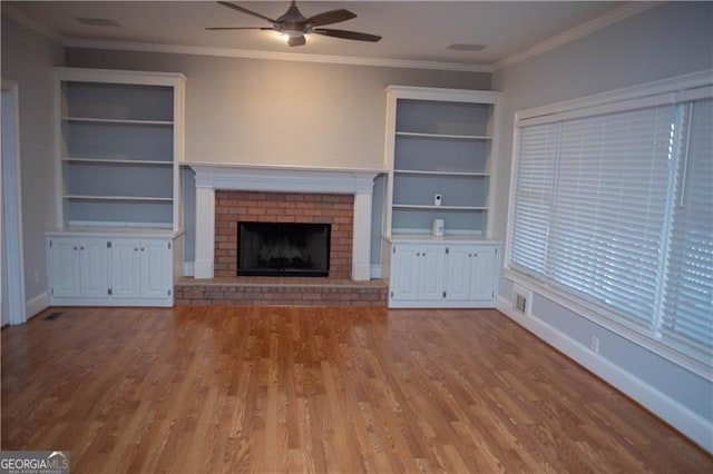 unfurnished living room featuring a fireplace, built in shelves, ceiling fan, and ornamental molding