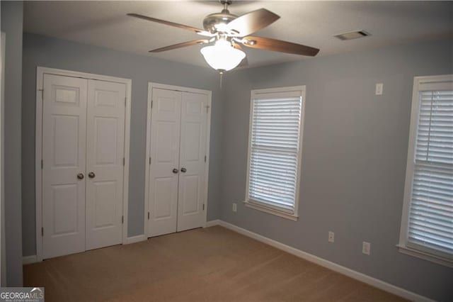 unfurnished bedroom featuring ceiling fan, carpet floors, and two closets