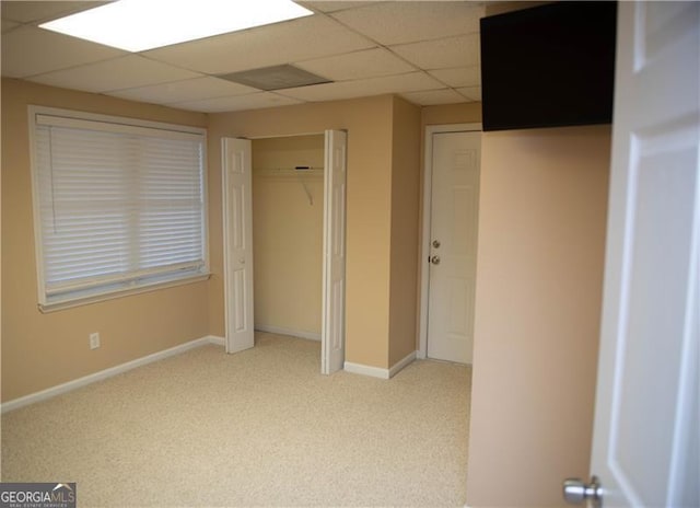 unfurnished bedroom with a paneled ceiling, light colored carpet, and a closet