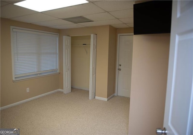 unfurnished bedroom with a paneled ceiling, a closet, and light colored carpet