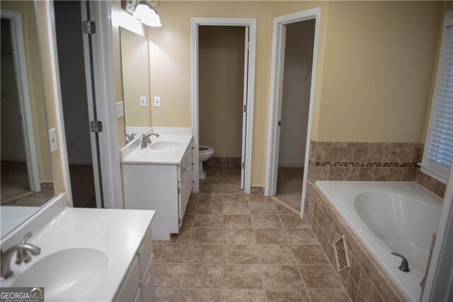 bathroom featuring vanity, a relaxing tiled tub, and toilet