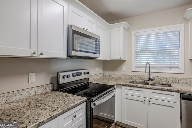 kitchen featuring appliances with stainless steel finishes, white cabinets, light stone countertops, and sink