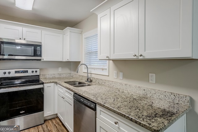 kitchen featuring wood-type flooring, stainless steel appliances, light stone counters, sink, and white cabinetry