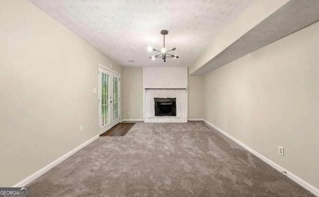 unfurnished living room with dark colored carpet, a large fireplace, a textured ceiling, and a chandelier