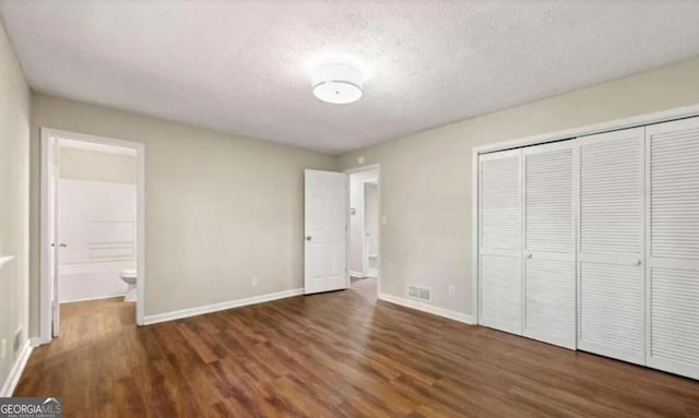 unfurnished bedroom featuring a textured ceiling, ensuite bath, a closet, and dark hardwood / wood-style flooring