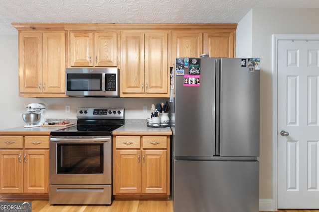 kitchen with a textured ceiling, stainless steel appliances, and light hardwood / wood-style flooring