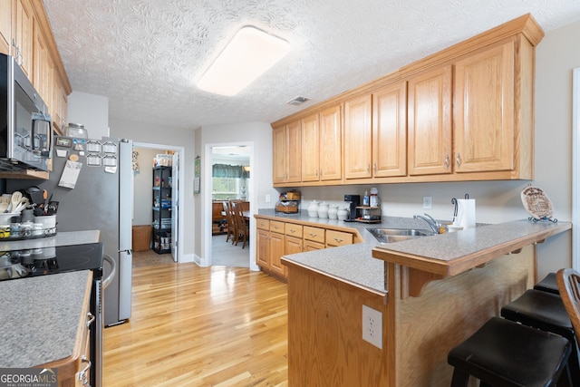 kitchen with sink, kitchen peninsula, a breakfast bar area, light brown cabinetry, and light wood-type flooring