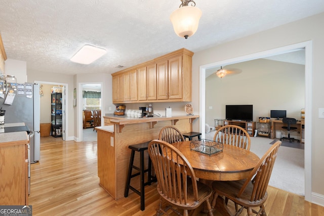 dining area featuring ceiling fan, light wood-type flooring, and a textured ceiling