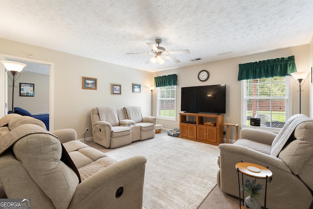 carpeted living room with a textured ceiling, ceiling fan, and a healthy amount of sunlight