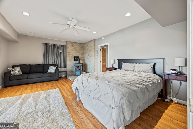 bedroom featuring light hardwood / wood-style floors, a wood stove, and ceiling fan