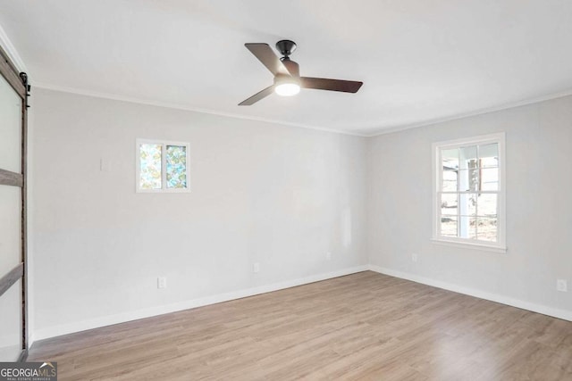 unfurnished room with a barn door, a wealth of natural light, light hardwood / wood-style floors, and ornamental molding