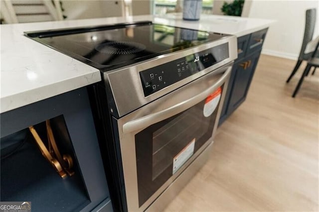 kitchen with stainless steel range oven, a fireplace, and light hardwood / wood-style flooring