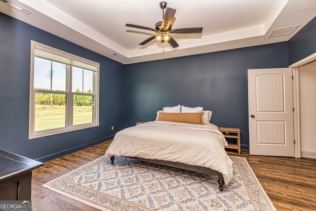 bedroom featuring ceiling fan, dark hardwood / wood-style flooring, and a raised ceiling