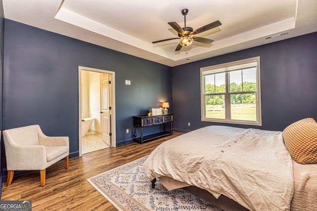 bedroom featuring a raised ceiling, ensuite bath, and hardwood / wood-style flooring