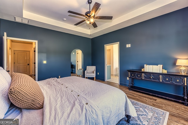 bedroom featuring wood-type flooring, connected bathroom, a tray ceiling, and ceiling fan