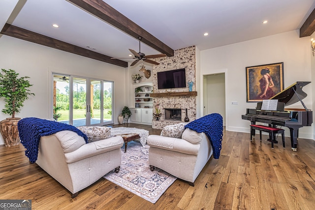 living room featuring ceiling fan, light hardwood / wood-style flooring, beamed ceiling, and a brick fireplace