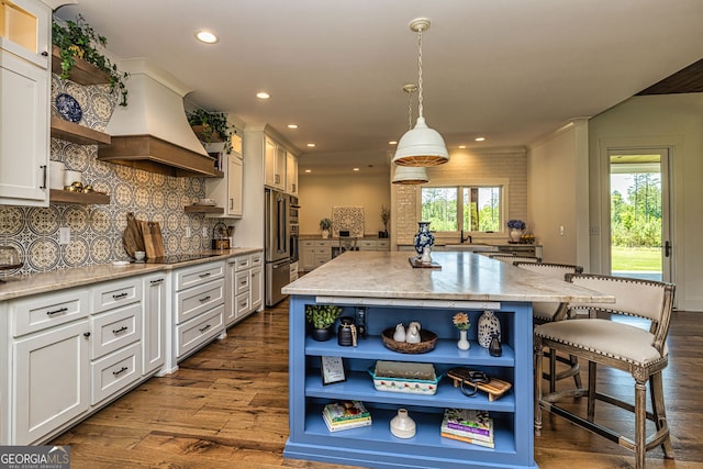 kitchen with premium range hood, light stone counters, white cabinets, a kitchen island, and hanging light fixtures