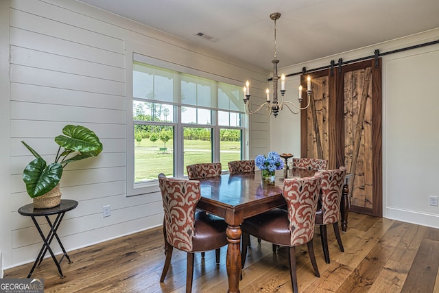 dining space featuring a barn door, wooden walls, wood-type flooring, and an inviting chandelier