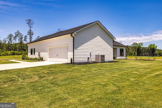 view of side of property featuring a lawn, a garage, a trampoline, and central AC