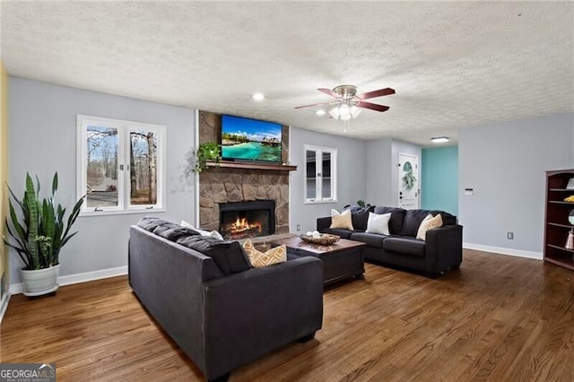 living room featuring a textured ceiling, a stone fireplace, ceiling fan, and dark wood-type flooring