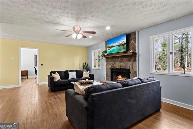 living room featuring ceiling fan, a stone fireplace, light wood-type flooring, and a textured ceiling