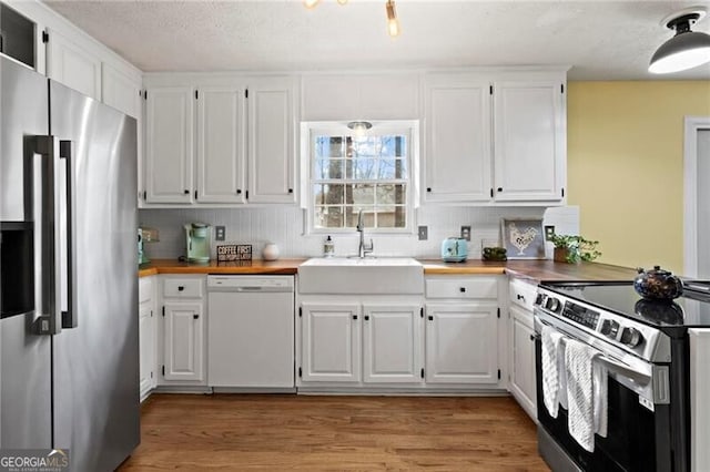 kitchen with butcher block counters, white cabinetry, sink, and appliances with stainless steel finishes