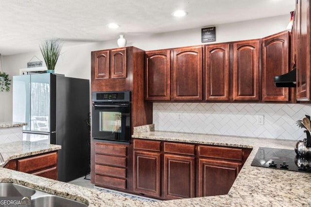 kitchen featuring decorative backsplash, light stone counters, extractor fan, sink, and black appliances