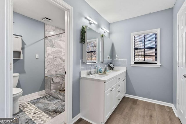 bathroom featuring vanity, toilet, a tile shower, and wood-type flooring