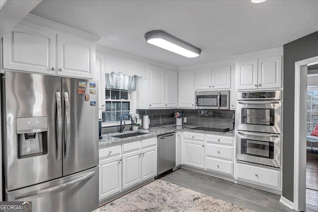 kitchen with white cabinetry, sink, stainless steel appliances, light stone counters, and backsplash