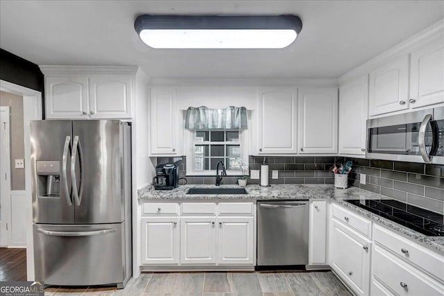 kitchen with sink, stainless steel appliances, light stone counters, backsplash, and white cabinets