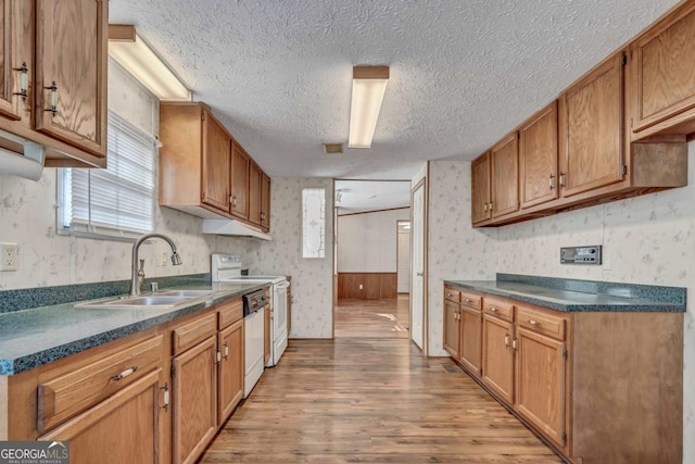 kitchen featuring a textured ceiling, white appliances, sink, light hardwood / wood-style flooring, and wood walls