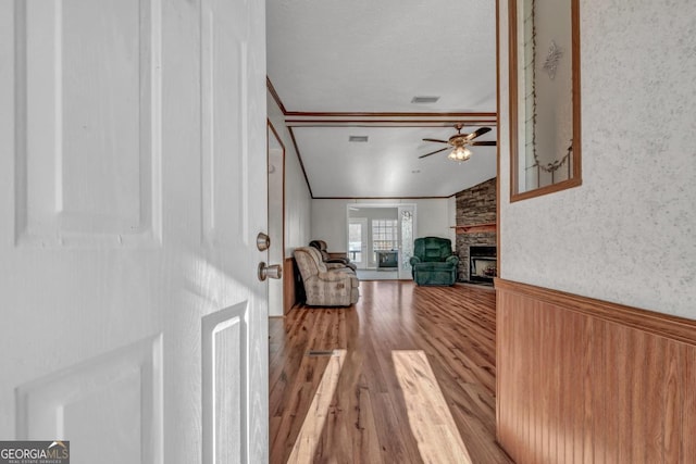 living room featuring ceiling fan, a large fireplace, crown molding, light hardwood / wood-style floors, and vaulted ceiling