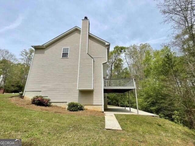 view of side of home featuring a wooden deck, a lawn, and a patio