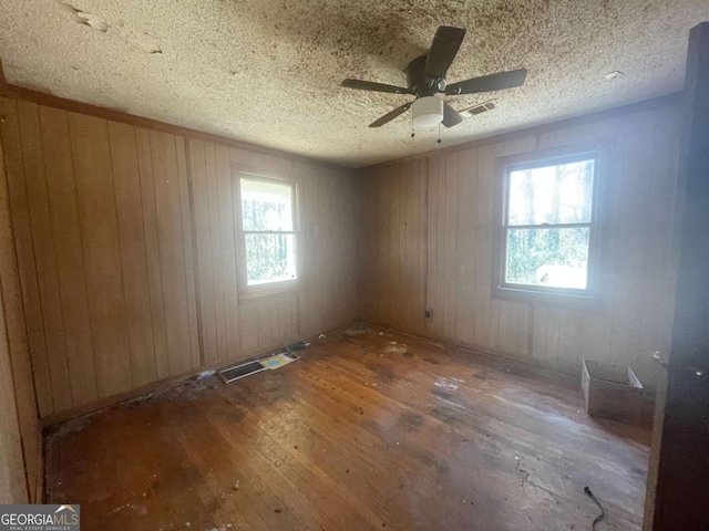 spare room with dark hardwood / wood-style flooring, plenty of natural light, wooden walls, and a textured ceiling