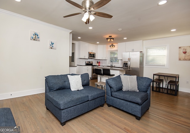 living room with light wood-type flooring, ceiling fan, crown molding, and sink