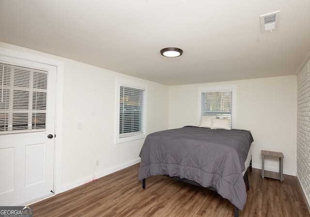 bedroom with dark wood-type flooring and brick wall